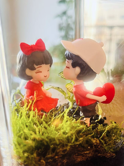 Two small figurines of a boy and girl in a decorative terrarium with plants. hand crafted by Lilli plants Dubai